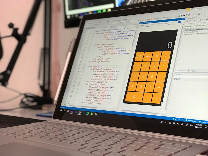 A close-up view of a laptop computer on a desk displaying lines of HTML or code in a text editor, alongside a calculator interface with orange buttons for fundamental functions such as addition, subtr